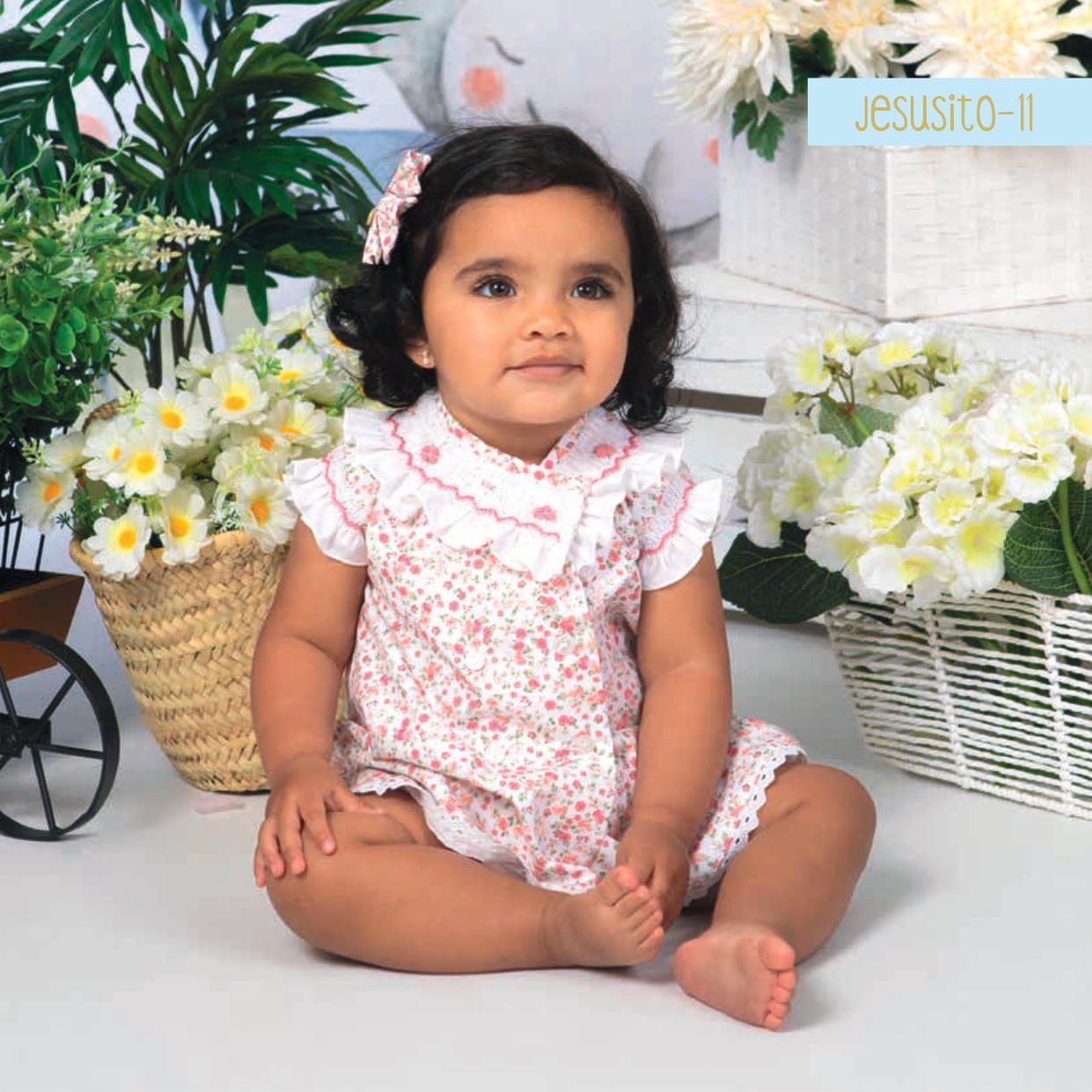 Vestido de bebé artesanal con nido de abeja bordado a mano y estampado floral coral sobre fondo crema